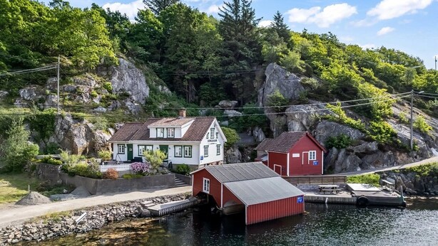 A waterfront property with a house and a red shed, surrounded by rocky terrain and greenery.