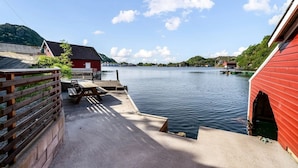 A lakeside dock with a red building, a wooden fence, and a picnic table.