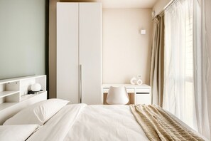 Una camera d'albergo con un letto, una scrivania, un armadio e una finestra con tende.