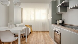Een moderne keuken met witte kastjes, een inbouwoven en een raam met dunne gordijnen.