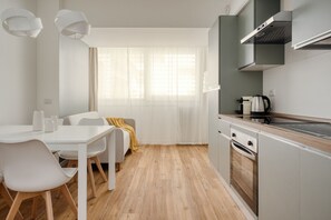 Eine moderne Küche mit weißen Schränken, einem Einbauofen und einem Fenster mit transparenten Vorhängen.