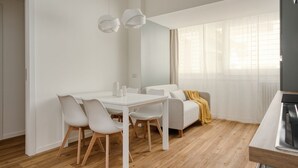Een moderne, minimalistische woonkamer met een eethoek, een bank en een televisie.
