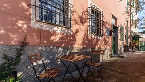 A patio with two wooden tables and chairs, a building with barred windows, and a narrow street. - GuestHost - A practical 20 square meters studio apartment, perfect for two people, located on the ground floor of a building with a private entrance.The property is located in the Nervi neighborhood, just 400 meters from Caprafico beach, making it easy f (Genoa)