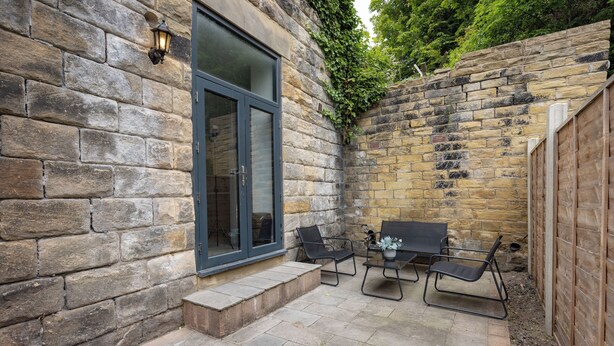 Un patio con paredes de piedra, puerta de cristal, mobiliario exterior y valla de madera.