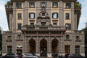 Un immeuble à plusieurs étages doté d’une entrée centrale, de portes en arc de cercle et de balcons ornés de plantes.