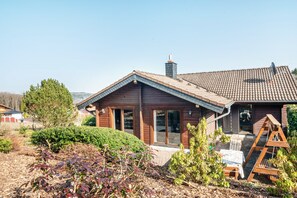 Ein Holzhaus mit Ziegeldach, Schornstein und einer Veranda mit Tisch und Stühlen.