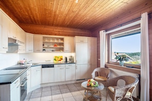 Eine Küche mit Holzausstattung, ein Essbereich mit Korbstühlen und ein Fenster mit Blick.