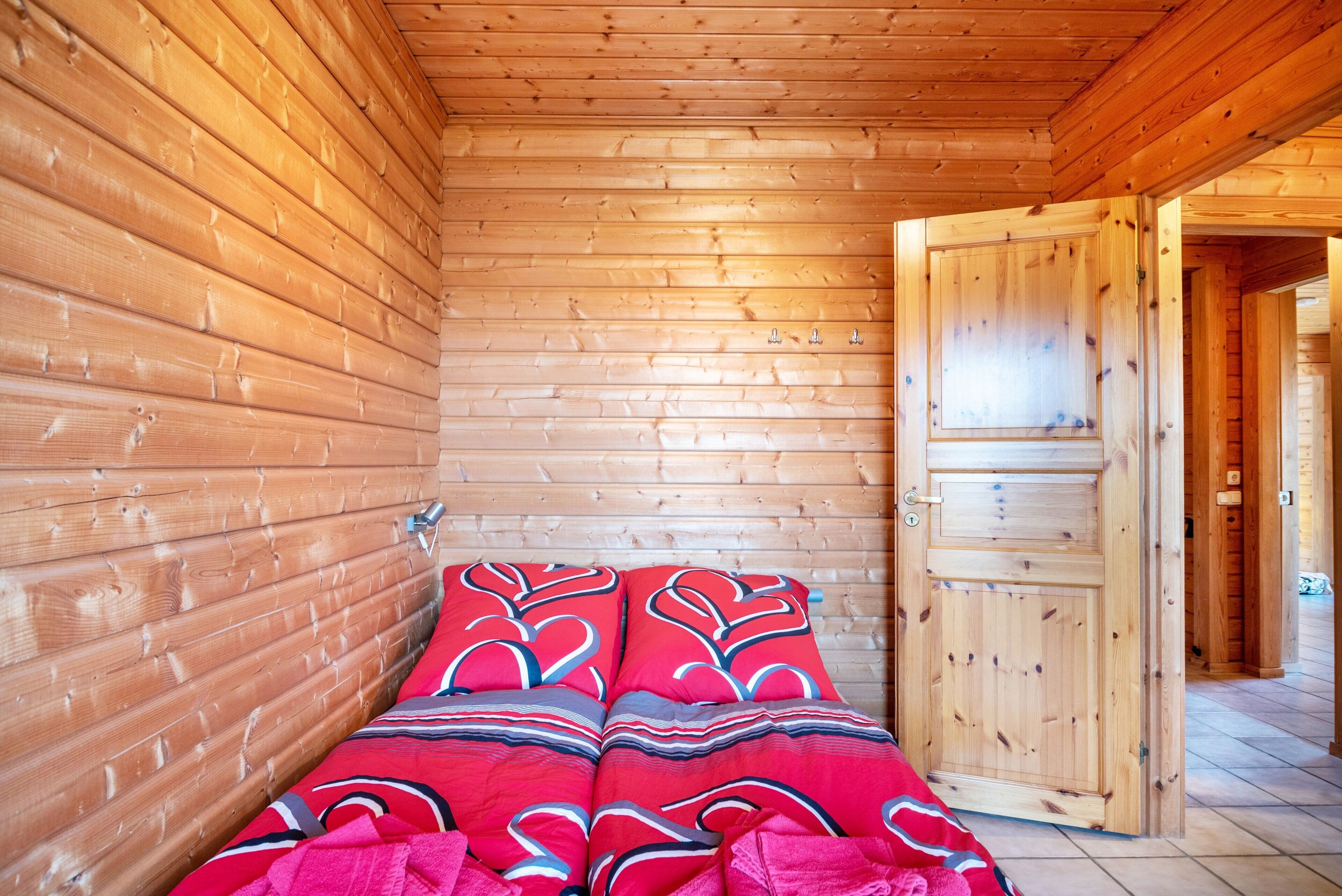 A wooden cabin interior with a bed, a door, and a tiled floor.