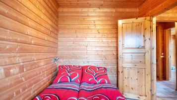 A wooden cabin interior with a bed, a door, and a tiled floor.