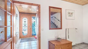 Ein Flur mit Holztüren, einer Glastür mit Buntglasfenster, einem Holzkasten, einem gerahmten Spiegel und einem Heizkörper.