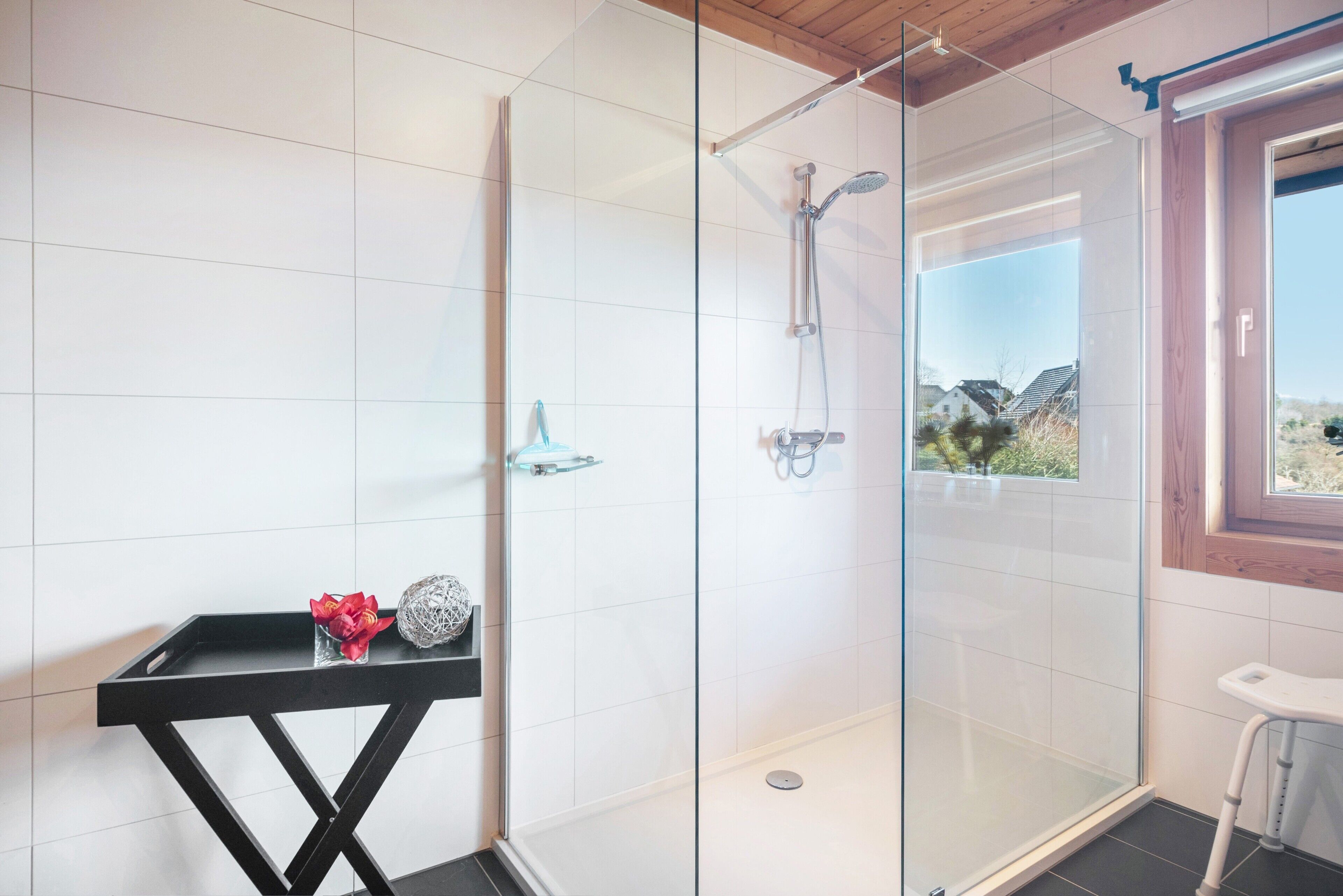 A modern bathroom with a glass shower enclosure, a black console table with decorative items, and a view of the outdoors through a window.