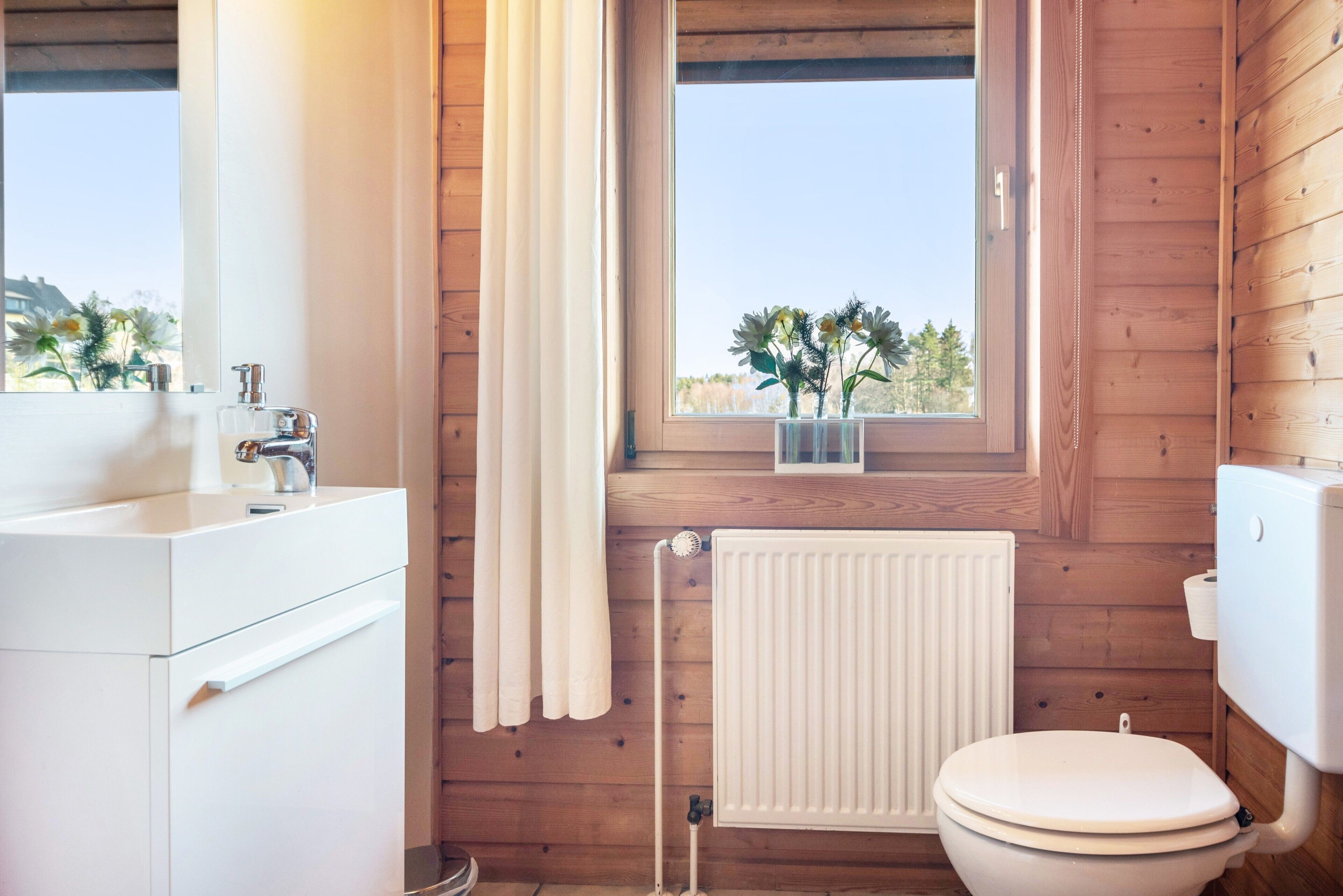 A wooden cabin bathroom with a white sink, toilet, and radiator.