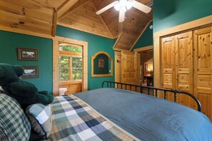 A bedroom with a bed, a large teddy bear, wooden walls, a ceiling fan, and a window. - Among the Clouds: Stay High Above It All (Gatlinburg)