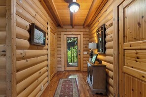 A log cabin interior with a wooden floor, a door with a glass panel, a mounted map, a small table with a lamp, and a ceiling light fixture. - Among the Clouds: Stay High Above It All (Gatlinburg)