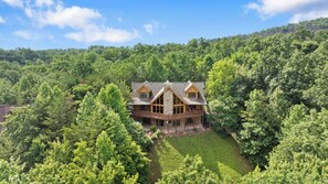 A large, two-story house with a stone foundation and wooden exterior, surrounded by dense forest. - Among the Clouds: Stay High Above It All (Gatlinburg)