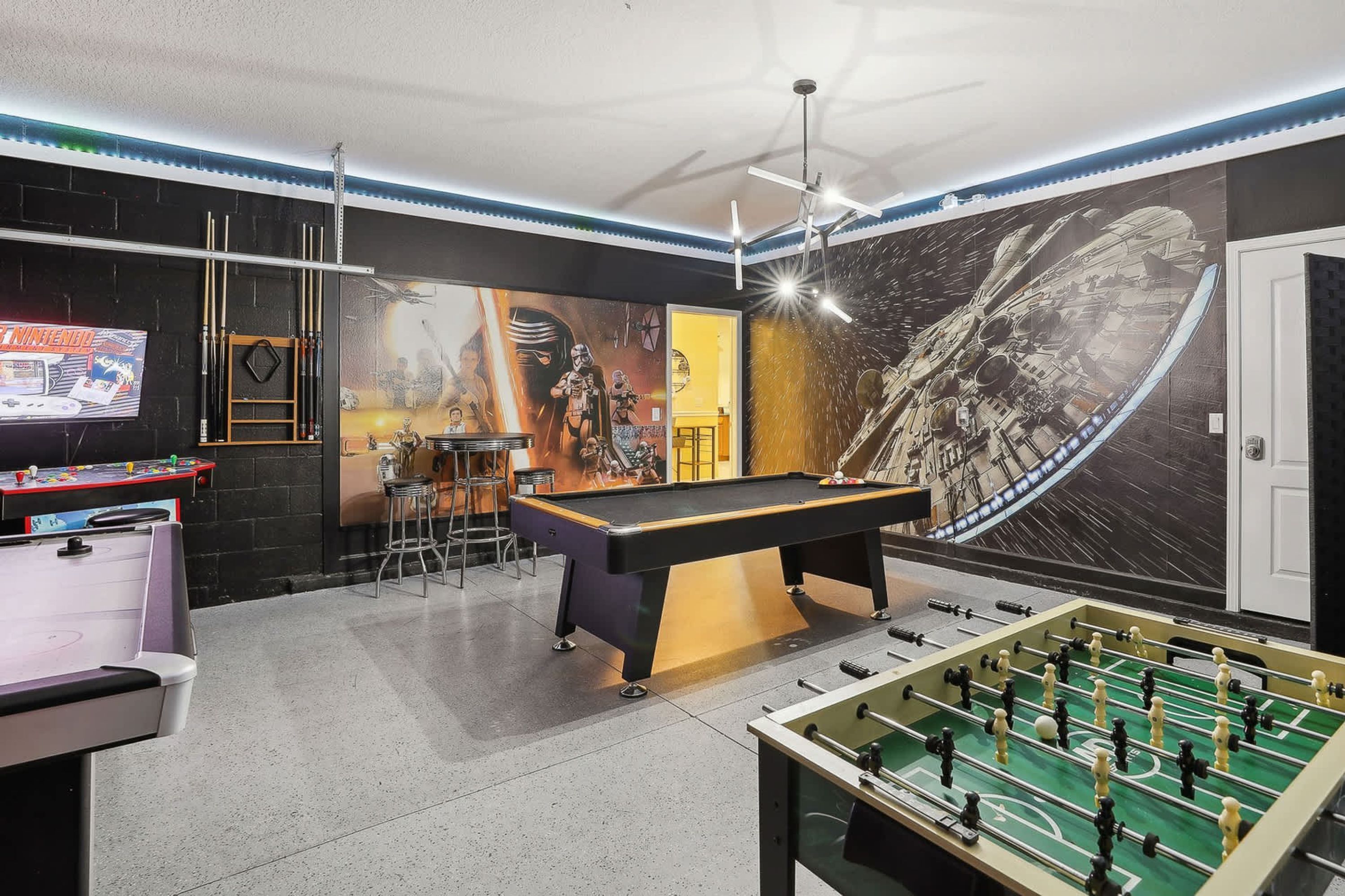 Une pièce équipée d’une table de billard, d’un baby-foot et d’un bar avec des tabourets.