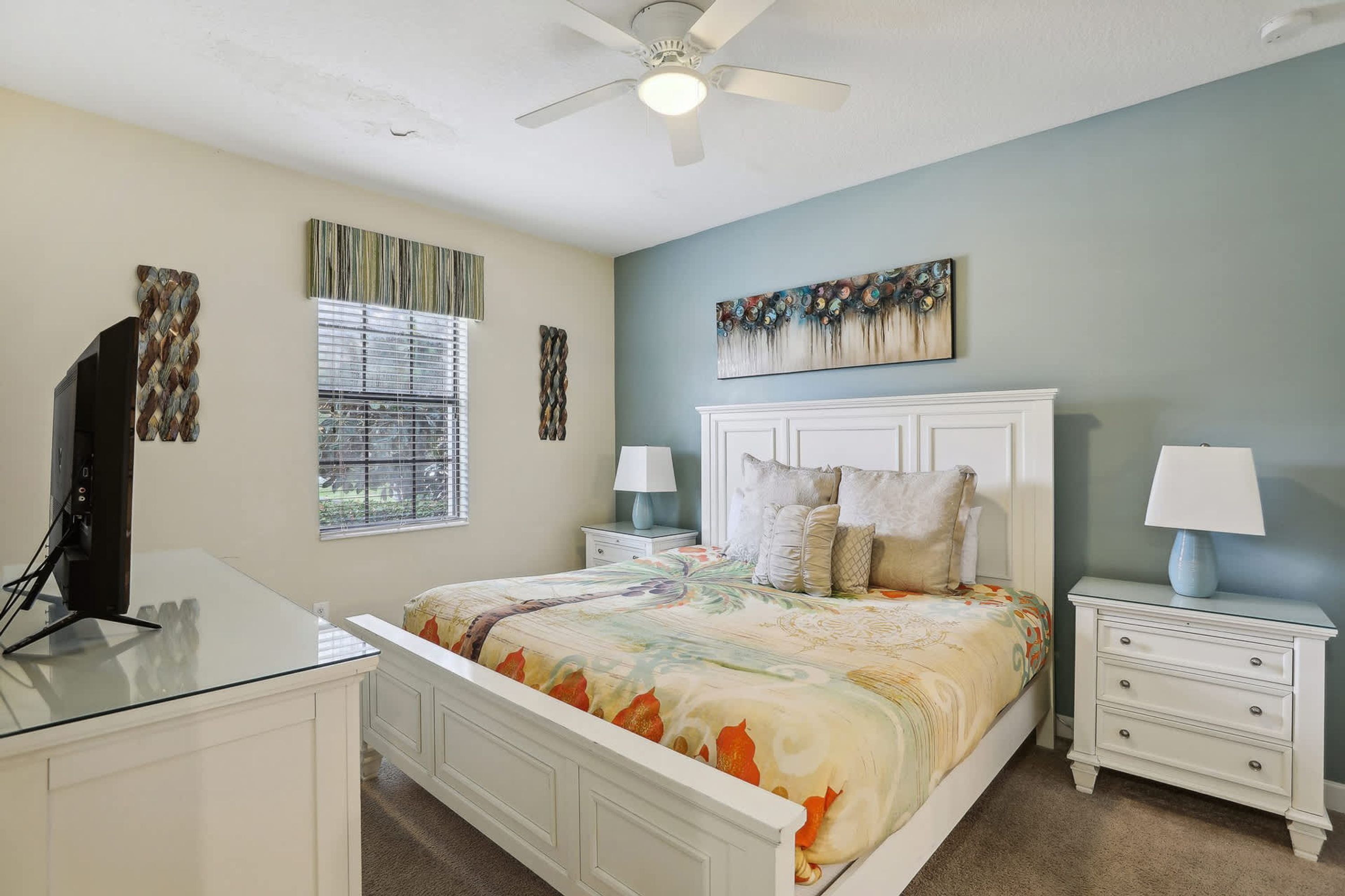 A bedroom with a bed, a nightstand, a TV, and a ceiling fan.