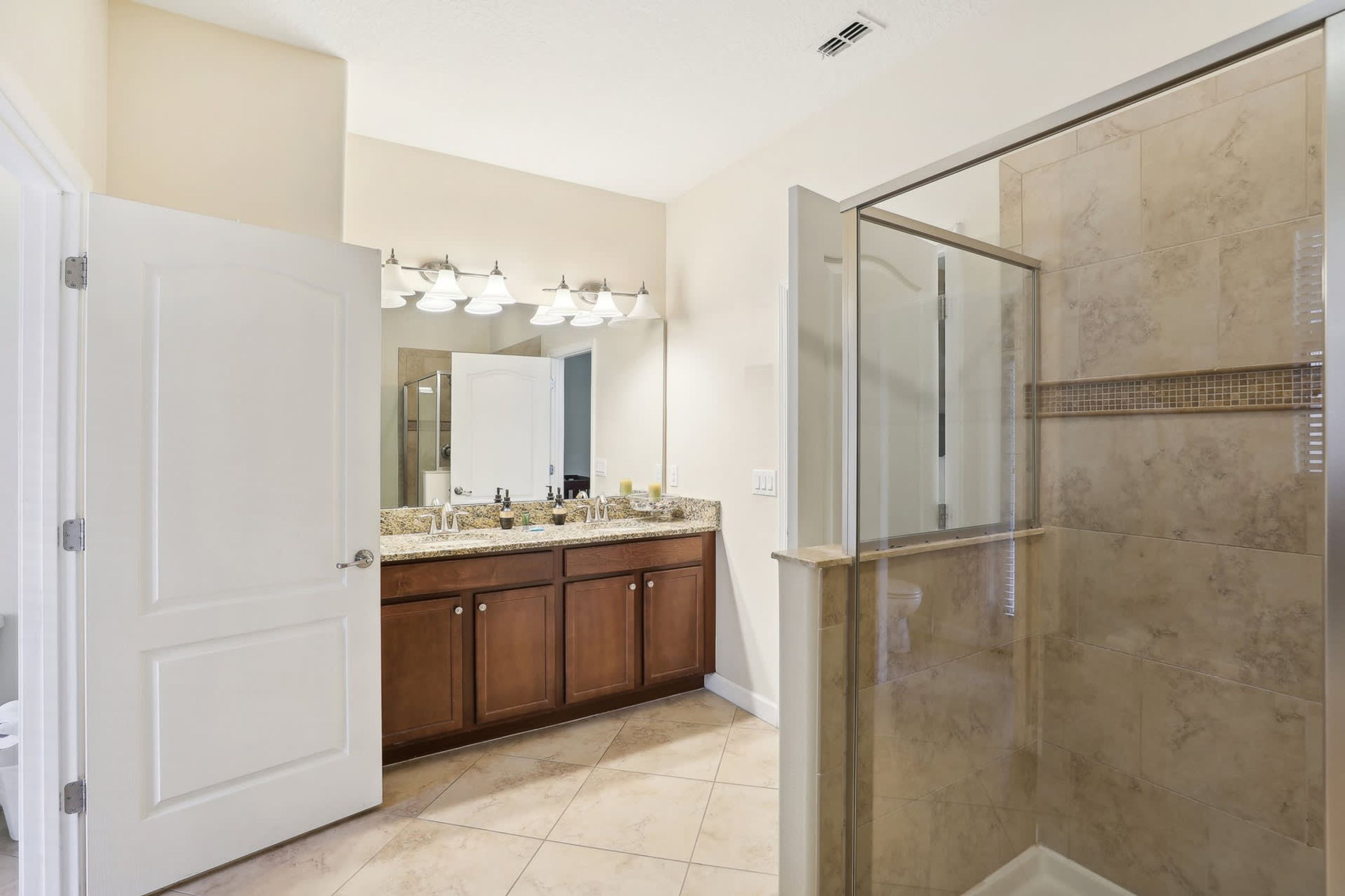 A bathroom with a shower, a vanity with a mirror, and a door leading to another room.