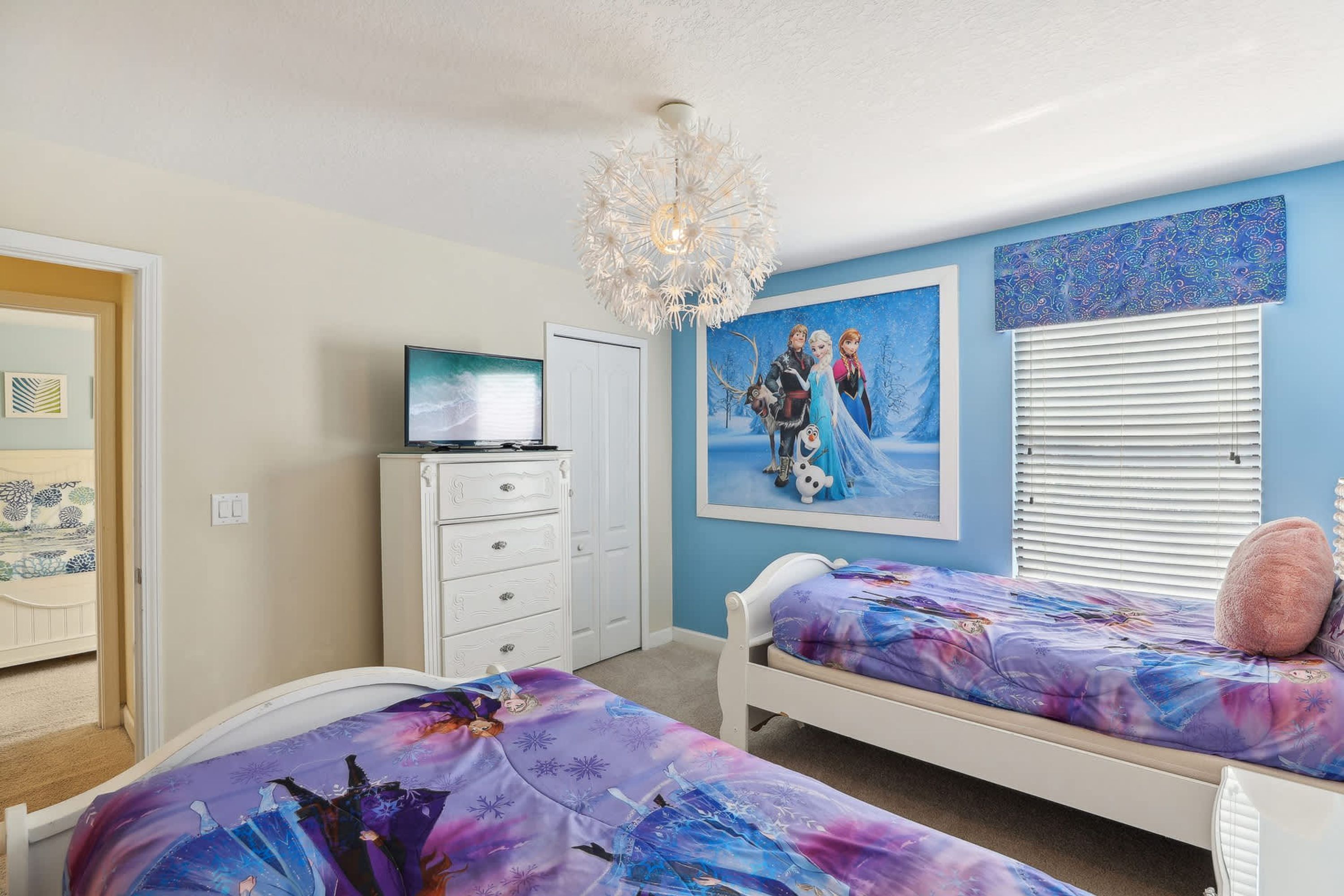 Une chambre avec deux lits, une télévision, une commode et un lustre.