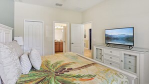 Ein Schlafzimmer mit Bett, Fernseher, Deckenventilator und Blick auf eine Küche und ein Badezimmer durch eine offene Tür.