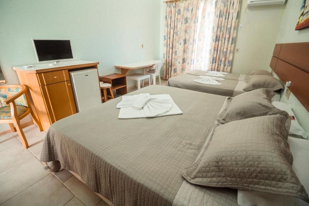 Una habitación de hotel con dos camas, un escritorio, una silla, un televisor y un refrigerador pequeño.