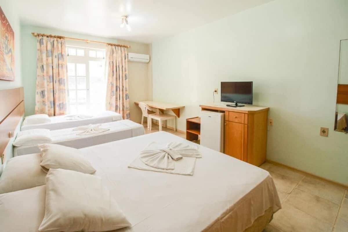 Quarto de hotel com duas camas, uma escrivaninha, televisão e guarda-roupa.