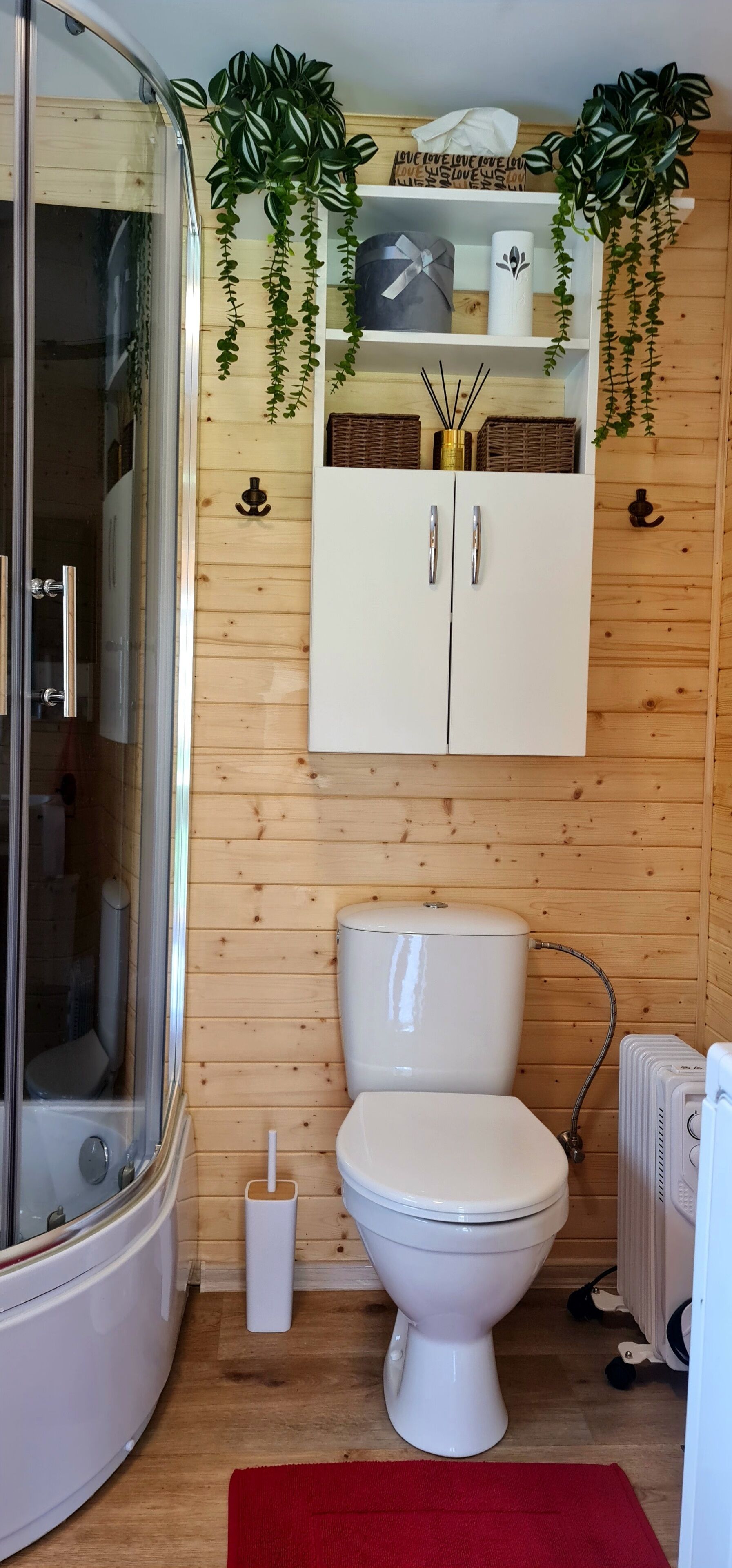Ein Badezimmer mit Duschkabine aus Glas, einer weißen Toilette, einem weißen Schrank mit einer goldenen Vase und Holzverkleidung.
