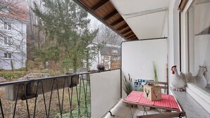 Een balkon met een tafel, stoelen en uitzicht op een tuin en omliggende huizen.