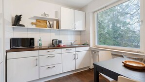 Een moderne keuken met witte kastjes, een magnetron, een koffiezetapparaat en een raam met uitzicht op bomen.