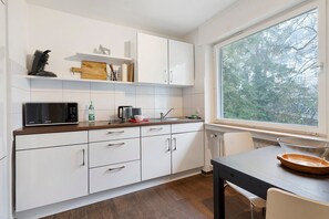 A modern kitchen with white cabinets, a microwave, a coffee maker, and a window with a view of trees. - Apartment "City, 38 sqm" with Balcony and Wi-Fi (Baden-Baden)