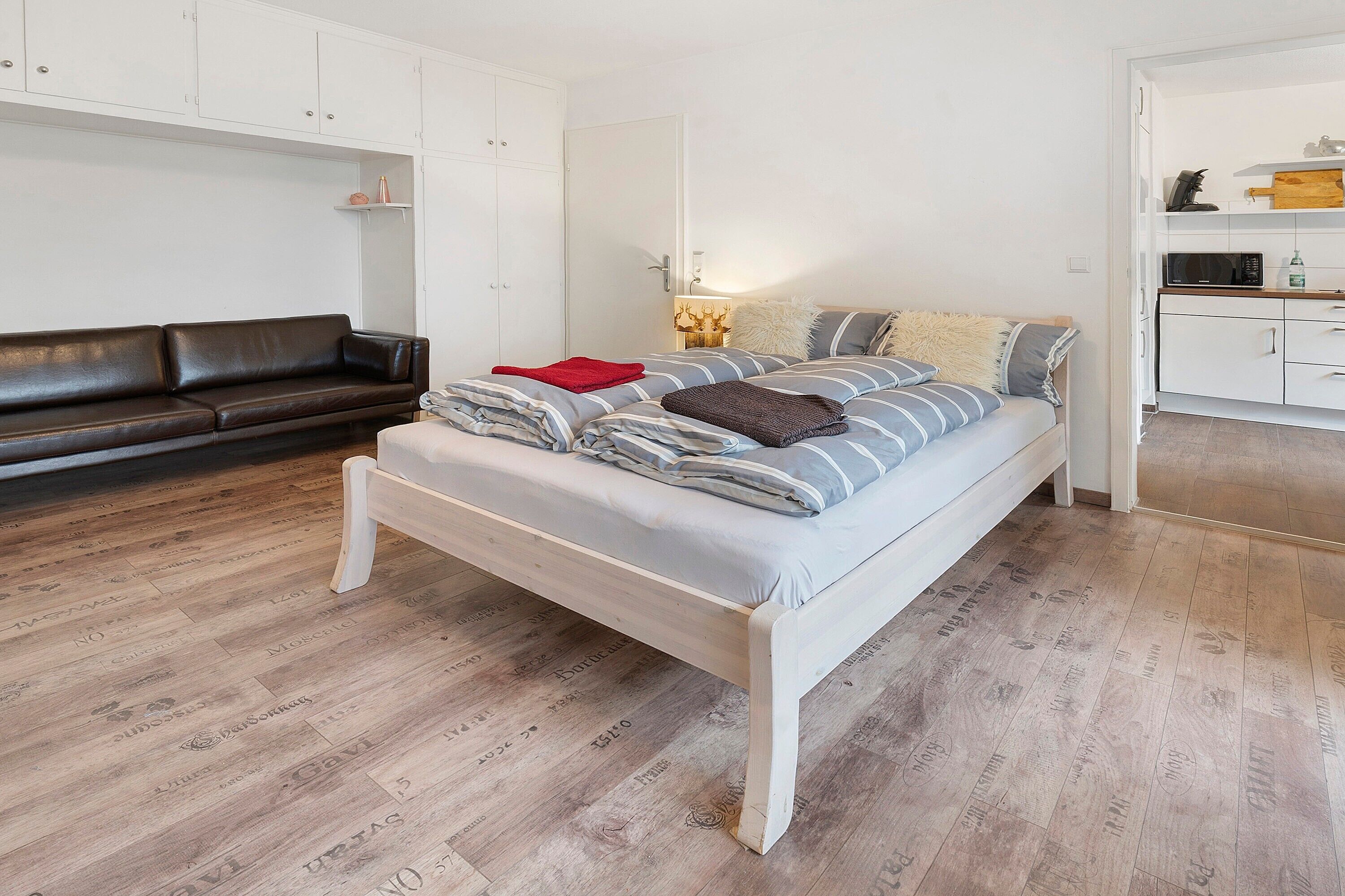 A bedroom with a bed, a white wardrobe, a brown leather sofa, and a wooden floor.