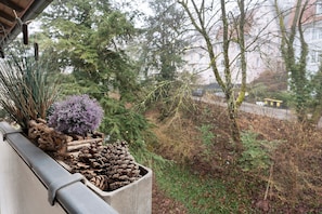 A concrete planter with pinecones, a small purple plant, and dried reeds on a balcony. - Apartment "City, 38 sqm" with Balcony and Wi-Fi (Baden-Baden)