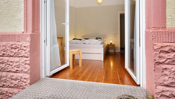 An open doorway leading to a bedroom with a bed, a small wooden stool, and a nightstand with a lamp. - Apartment, 33 sqm, up to 2 guests with private terrace and Wi-Fi (Baden-Baden)