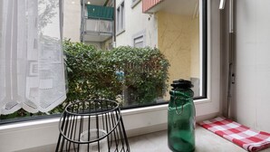 A window with a lace curtain, a metal chair, a green bottle, and a checkered towel on a windowsill. - Apartment, 33 sqm, up to 2 guests with private terrace and Wi-Fi (Baden-Baden)