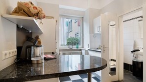 A kitchen with a coffee maker, a window with a view of buildings, and a checkered floor. - Apartment, 33 sqm, up to 2 guests with private terrace and Wi-Fi (Baden-Baden)