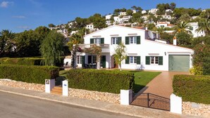 Una villa bianca con un balcone, un garage e un giardino curato.