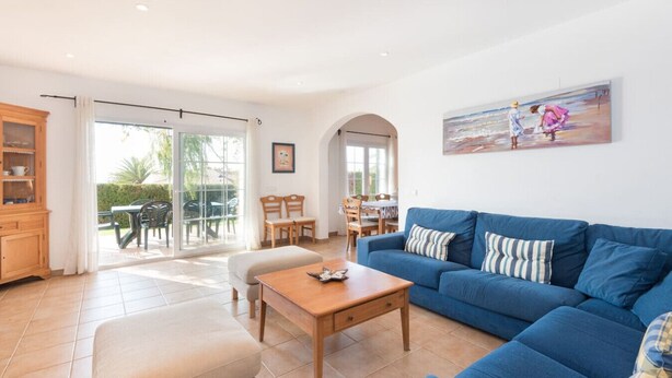 Un'ampia zona giorno con un divano blu, un tavolino in legno e un tavolo da pranzo con sedie. Una porta vetrata scorrevole dà accesso a una terrazza esterna.