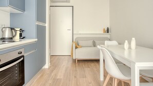 A modern kitchen with a stove, oven, and kettle, a dining area with a white table and chairs, and a grey sofa. - Hostmate - Milano - Imperia's Pearl - Romolo IULM (Milano)