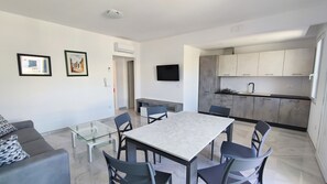 A modern living space with a dining area, kitchen, and a flat-screen TV mounted on the wall. - Apartment 'Nuovo T San Giovanni' with Private Terrace, Balcony and Air Conditioning (Torre San Giovanni)