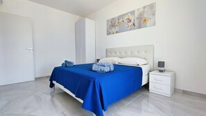 Een slaapkamer met een bed, nachtkastje, lamp en een schilderij van bloemen aan de muur.