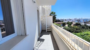 En balkon med gelænder i hvidt, en spiraltrappe og udsigt over det omkringliggende kvarter.