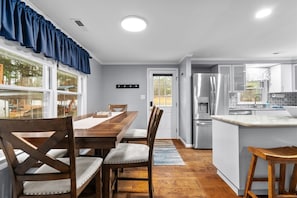 A modern kitchen with a central island, stainless steel appliances, and a dining area with wooden furniture. - Lizard Creek Retreat | Pet-Friendly | New Boathouse (Littleton)