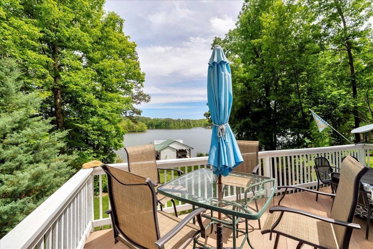 Eine Terrasse mit Gartenmöbeln, darunter Stühle und ein Tisch, mit Blick auf einen See.