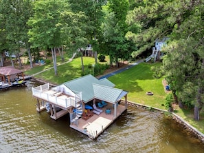 Ein schwimmendes Haus mit Deck, Sitzgelegenheit im Freien und einer kleinen Bootsanlegestelle.