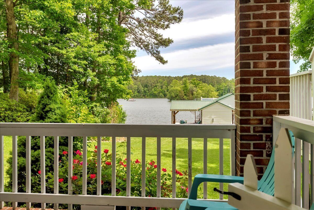 A porch with a view of a lake, surrounded by trees and a brick wall.