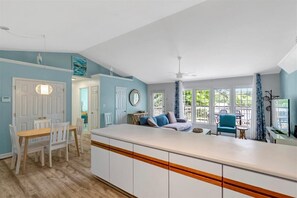 Eine Küche mit Kochinsel, Essbereich mit Stühlen, Deckenventilator und großen Fenstern.
