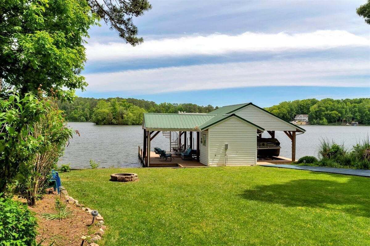 A lakeside cabin with a covered deck, a fire pit, and a view of the lake and forest.