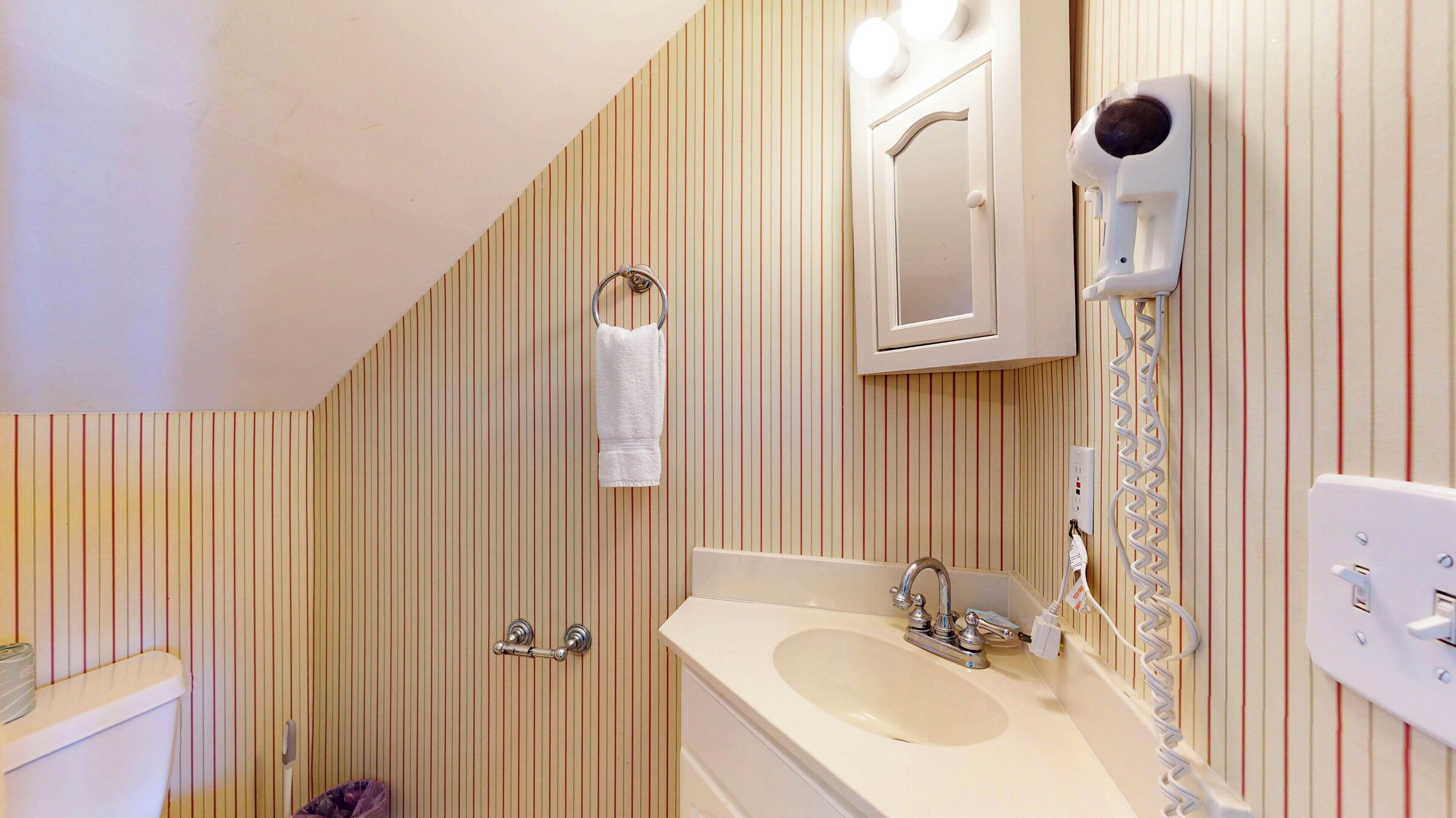 Ein Badezimmer mit Streifenmuster-Tapete, einem Waschbecken, einem Spiegel, einem Handtuchhalter und einem Föhn.