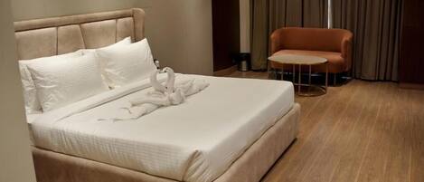 Una cama bien hecha con cabecera, una mesita redonda pequeña y un sofá en una habitación moderna con suelo de madera.