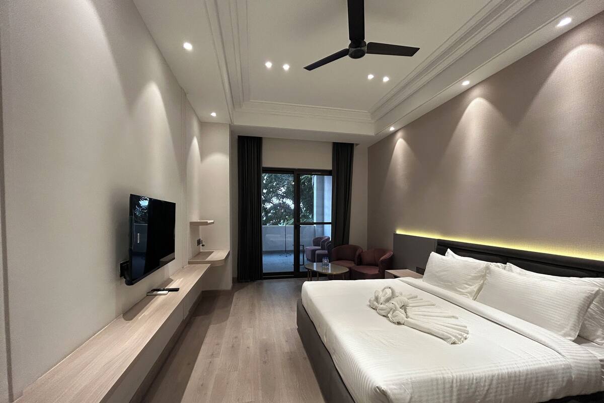 Una habitación de hotel moderna con una cama, un televisor, una zona de estar con sillas y un ventilador de techo.